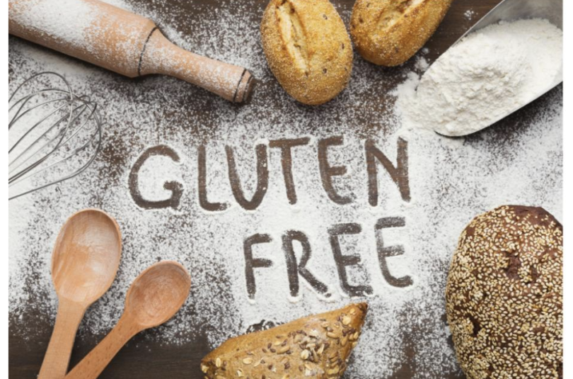 Gluten-free breads, flour, and a rolling pin on a table with 'GLUTEN FREE' written in flour, highlighting gluten-free baking ingredients. Gluten Free Diet Shopping Guide